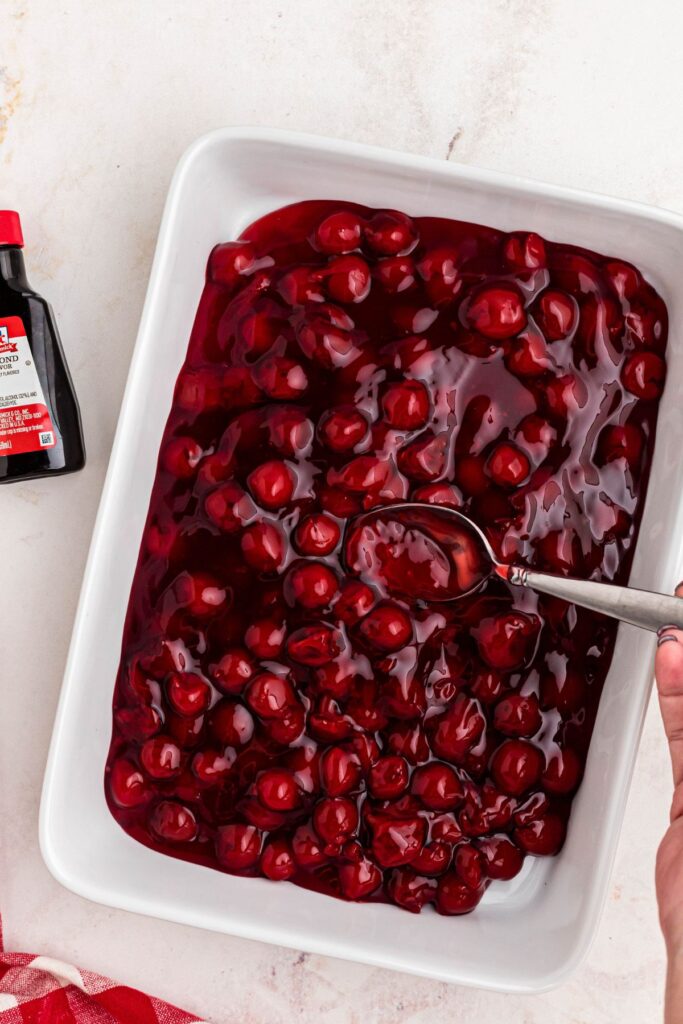 Cherry pie filling spread in a white casserole dish, mixed with almond extract. 