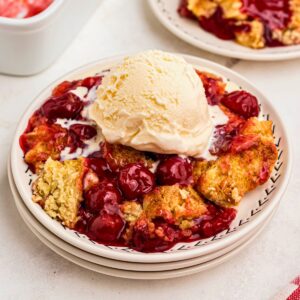 Golden crusted cherry dump cake on white plates topped with vanilla ice cream.