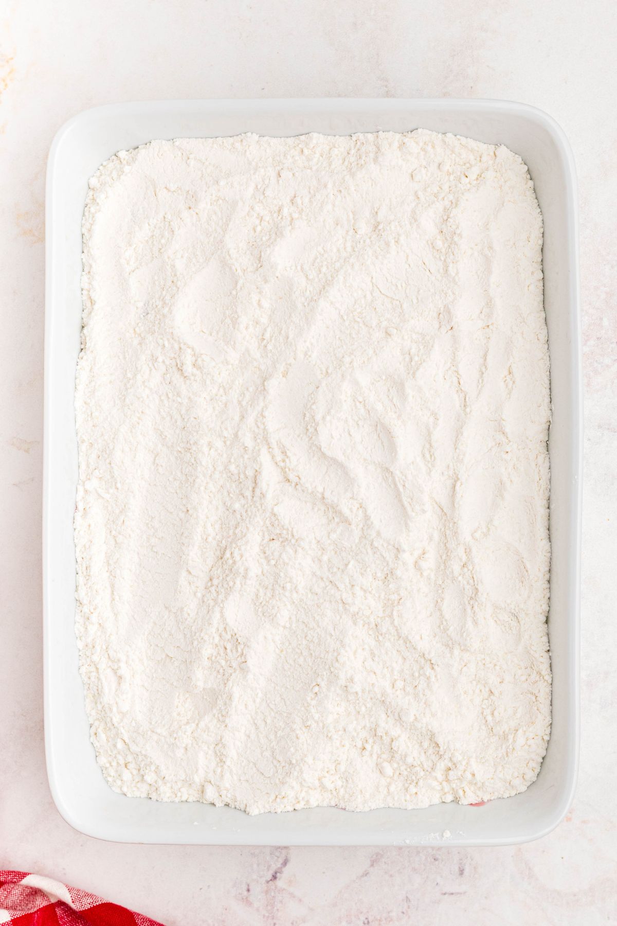 Cherries topped with yellow cake mix powder, in a white casserole dish before being baked.