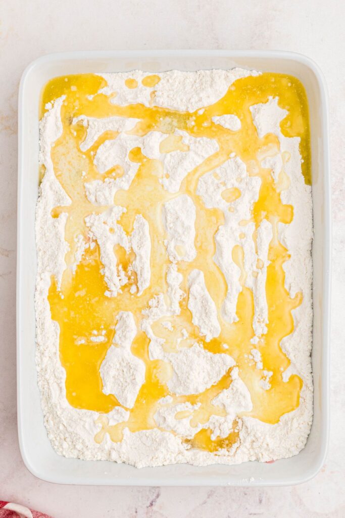 Melted butter poured over the yellow cake mix in a white casserole dish before baking in the oven. 