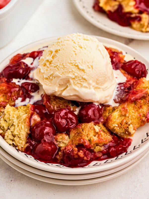 Golden crusted cherry dump cake on white plates topped with vanilla ice cream.