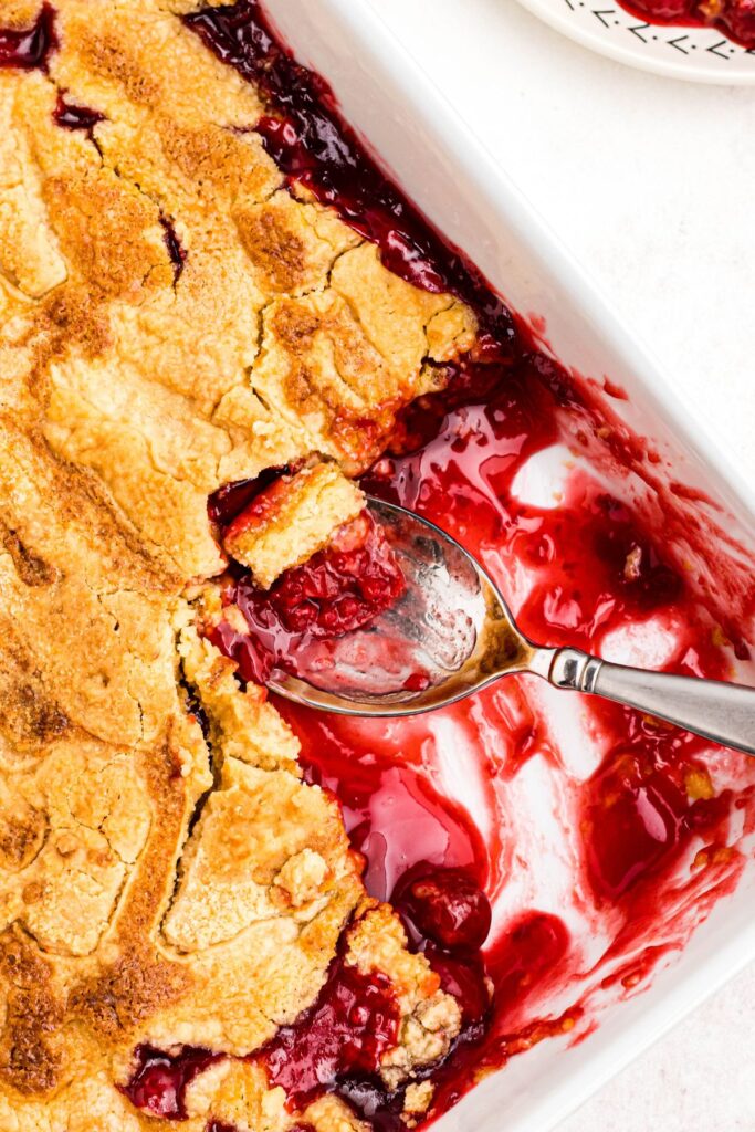 Cherry dump cake in a casserole dish with a serving scooped out and a spoon in the dish. 