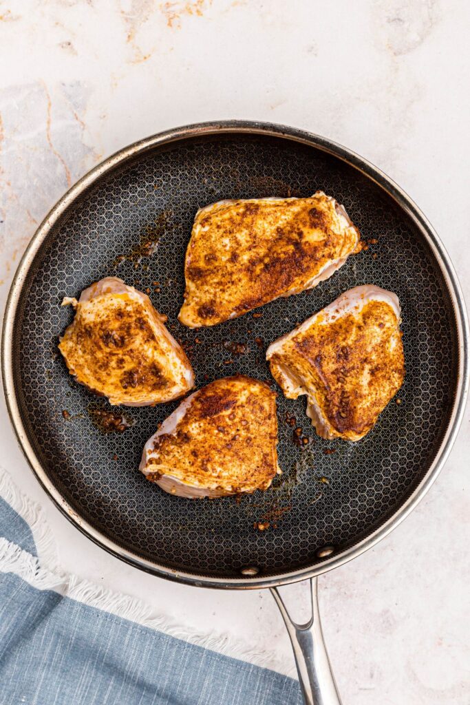 Golden seasoned seared chicken breast in a large skillet.