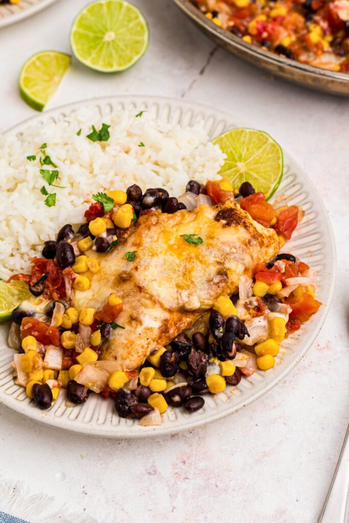 Juicy, cheese chicken surrounded by veggies, and served with rice on a white plate. 