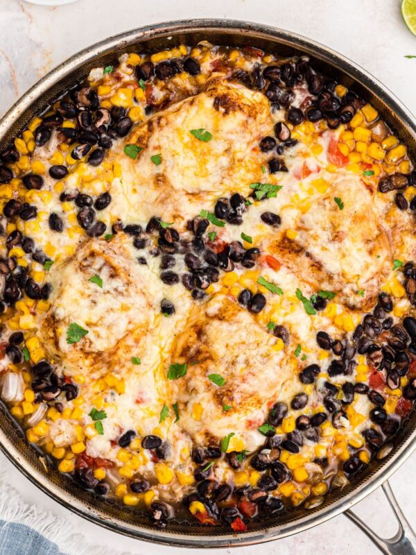 Golden cheesy chicken in a large skillet surrounded by black beans, corn, and tomatoes.