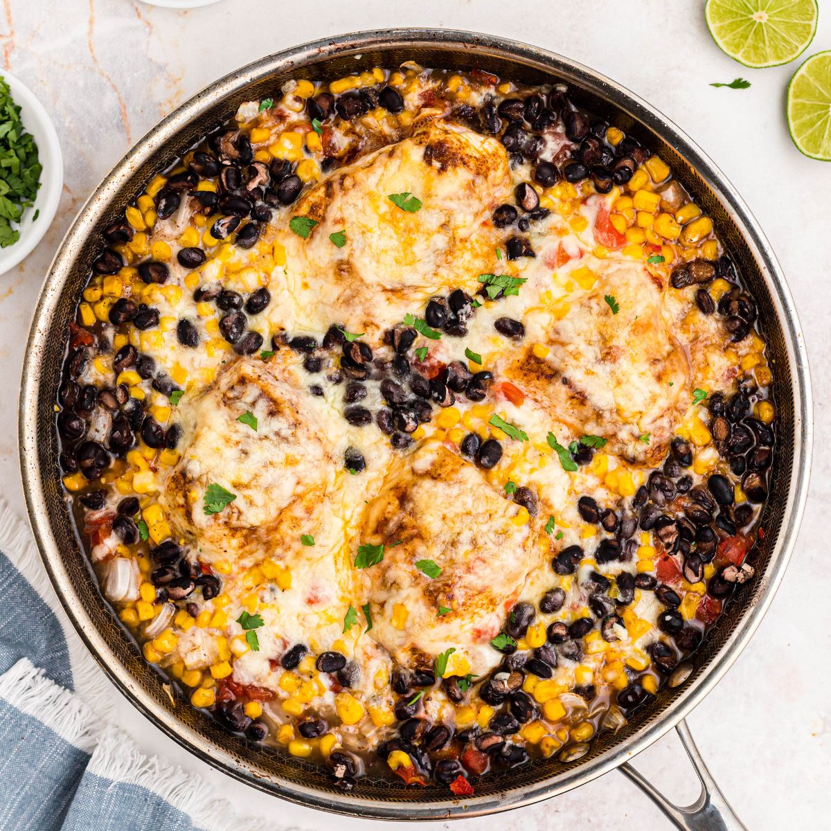 Golden cheesy chicken in a large skillet surrounded by black beans, corn, and tomatoes.