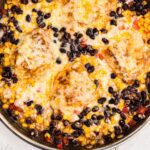 Chicken covered in cheese, beans, and veggies, in a large skillet.