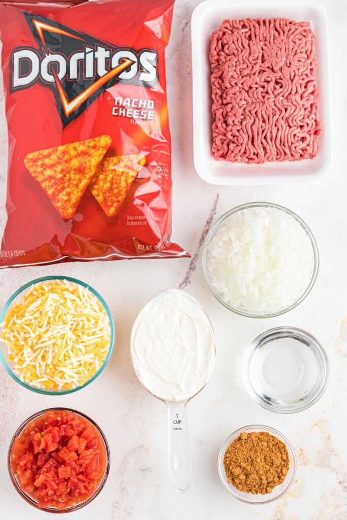 Ingredients needed to make Dorito casserole, measured in clear glass bowls on a marble table. 