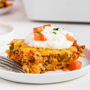 Cheesy meat and crushed Doritos, layered and cut into a slice on a white plate.