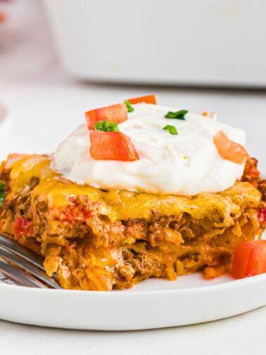 Cheesy meat and crushed Doritos, layered and cut into a slice on a white plate.