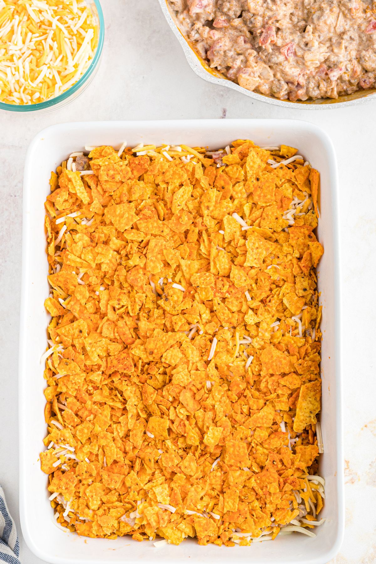White casserole dish covered with crushed Doritos and cheeses.