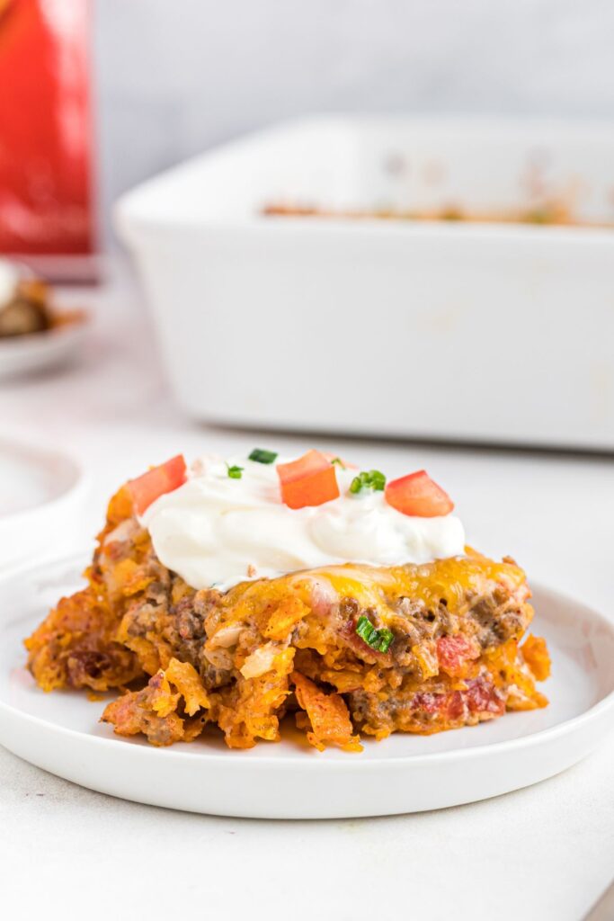 Cheesy Dorito casserole topped with sour cream on a white plate. 