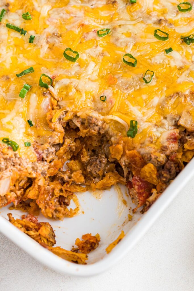 Cheesy Dorito casserole with ground beef in a white casserole dish, with a scoop missing. 