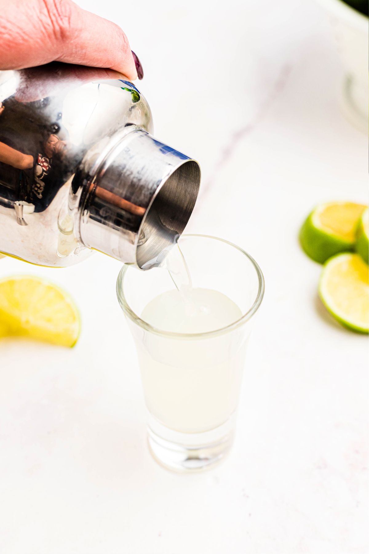 Alcohol being poured into shot glass from a cocktail shaker.