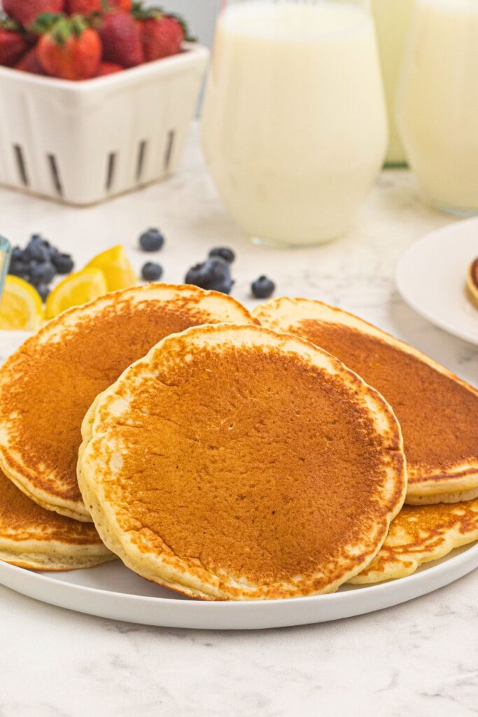 Stacked golden brown and fluffy pancakes on a white plate.