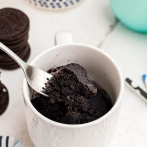 Chocolate mug cake with a bite scooped out on a fork with Oreos and milk on the table.