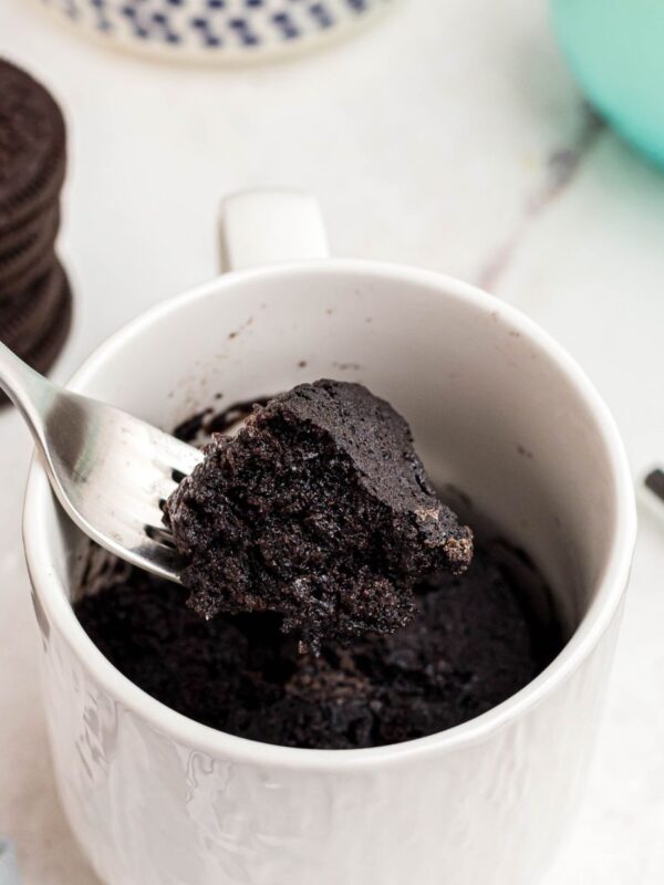 Chocolate mug cake with a bite scooped out on a fork with Oreos and milk on the table.