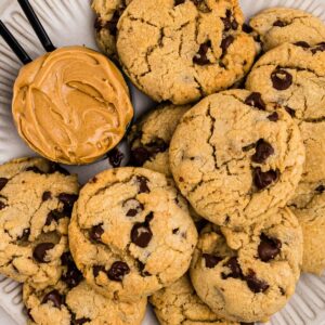 Peanut butter chocolate chip cookies on a white plate with a scoop of peanut butter next the cookies.