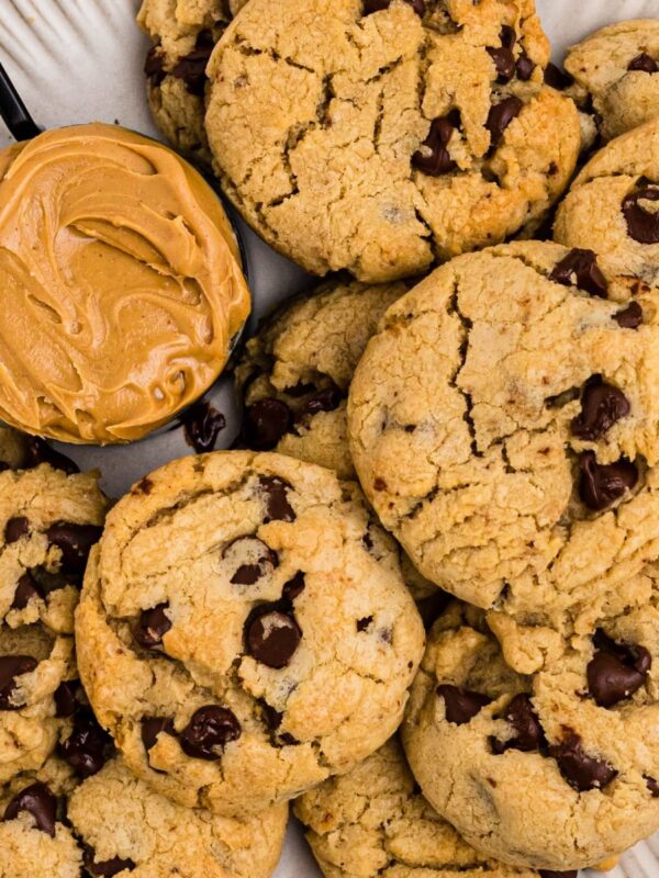 Peanut butter chocolate chip cookies on a white plate with a scoop of peanut butter next the cookies.