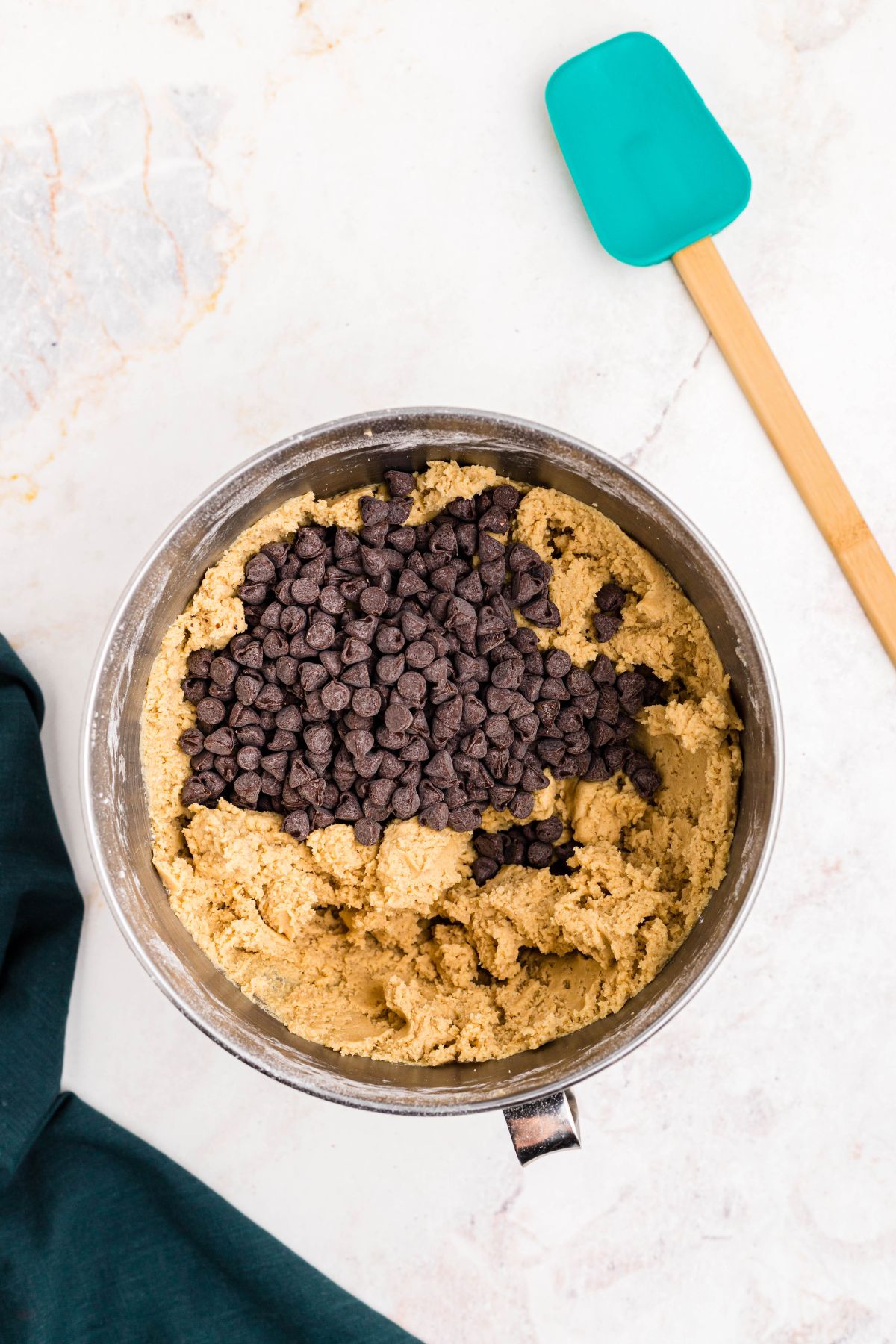 Cookie dough with chocolate chips on top, being mixed in a silver mixing bowl.
