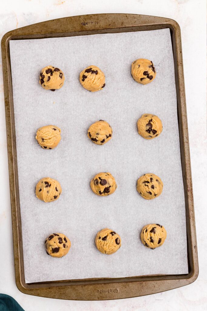 Peanut butter cookie dough scooped out and rolled into balls, placed on a baking sheet. 