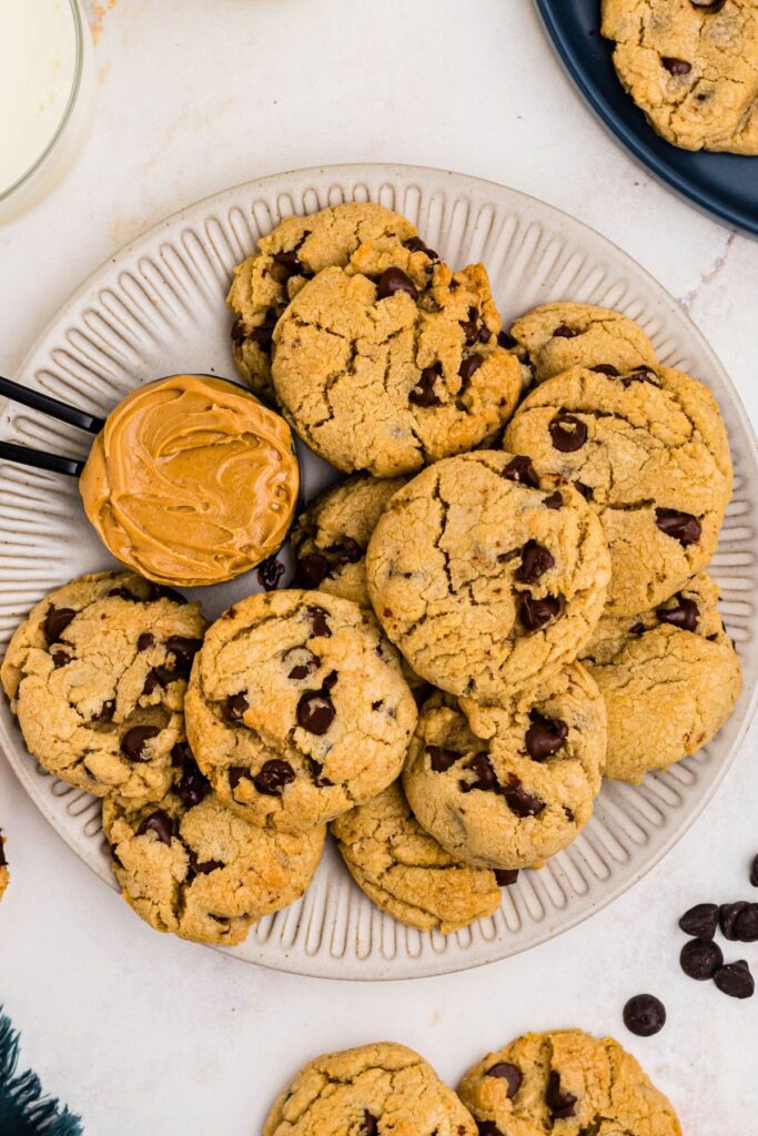 Golden soft peanut butter cookies with chocolate chips baked in, stacked on a white plate. 