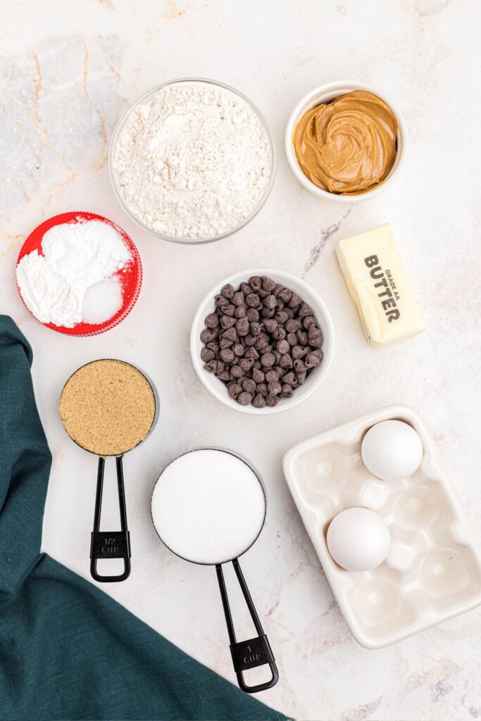 Ingredients needed to make peanut butter cookies with chocolate chips, measured on a white marble table. 