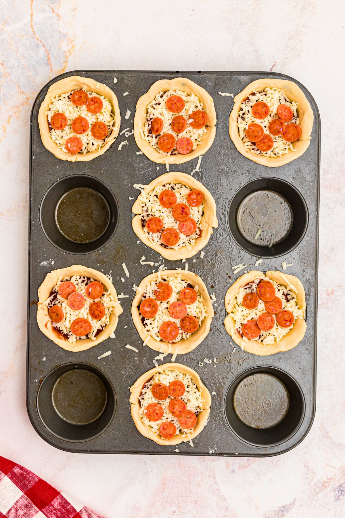 Muffin tin filled with crust dough, sauce, cheese, and pepperoni before being cooked.