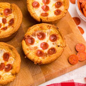 Golden crusted pizza cupcakes on a wooden cutting board with pepperoni scattered around the table.