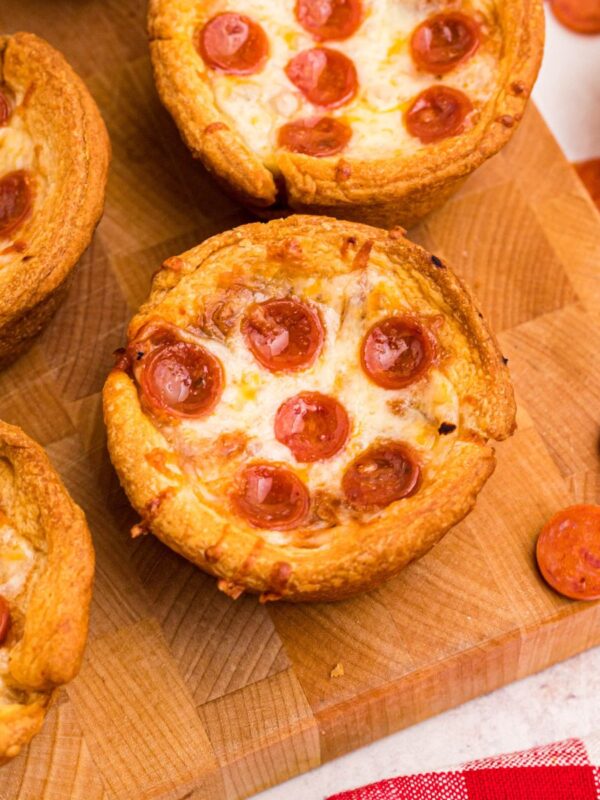 Golden crusted pizza cupcakes on a wooden cutting board with pepperoni scattered around the table.