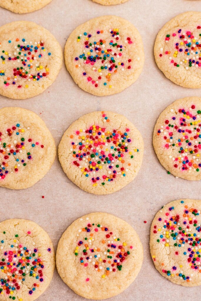 Baked sugar cookies with sprinkles on parchment paper.