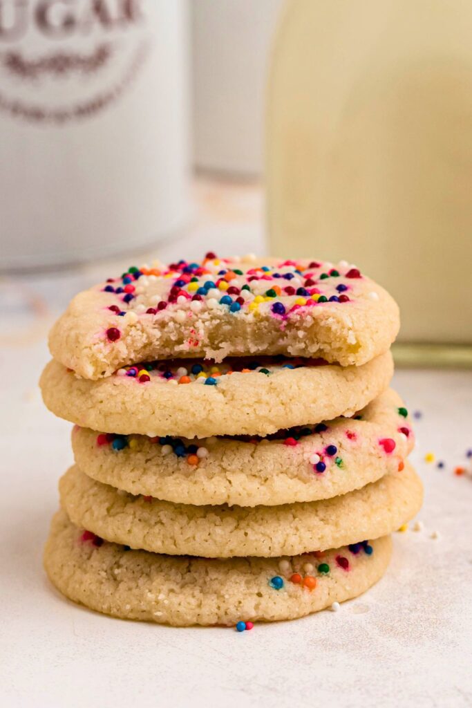 Small stack of sugar cookies with sprinkles, with the top cookie missing a bite. 