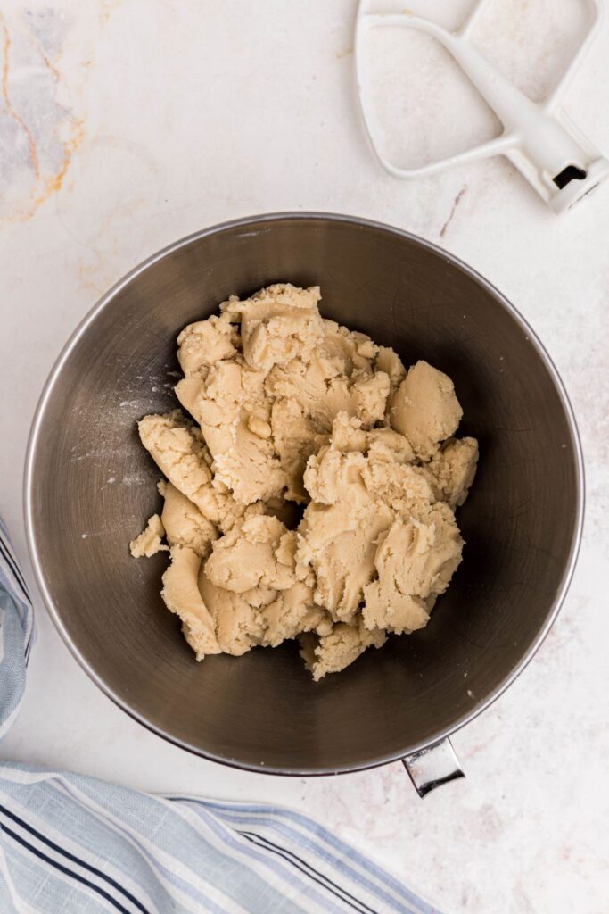 Soft dough in a mixing bowl with paddle attachment on the table next to it. 