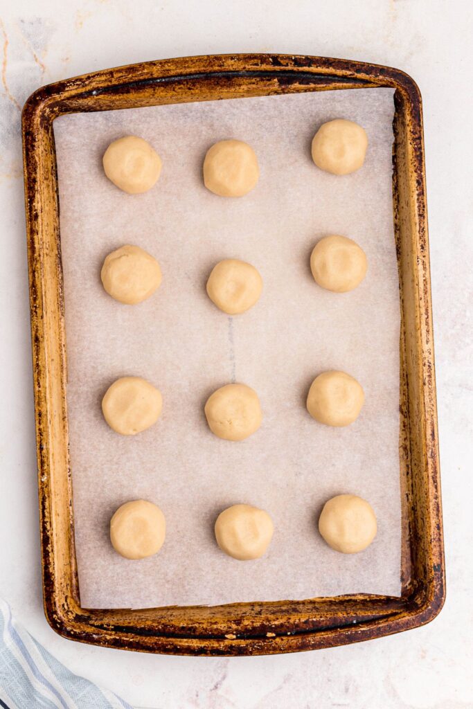 Rolled sugar cookie dough balls on a baking sheet lined with parchment paper. 