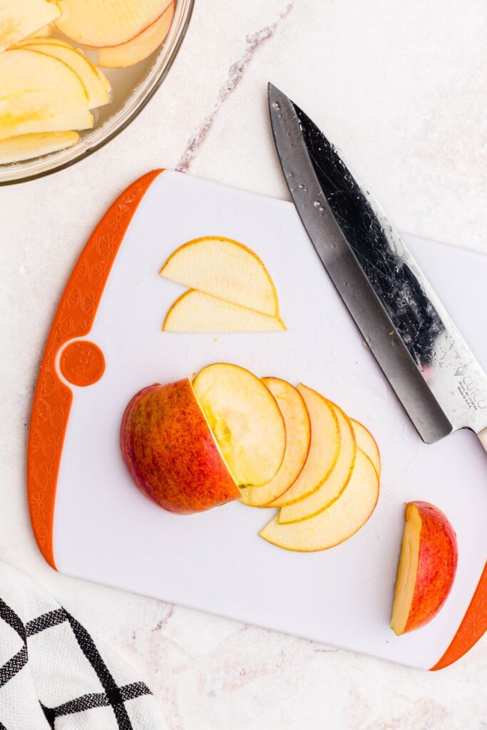 Apple being sliced on a cutting board and then being added to a bowl of water. 