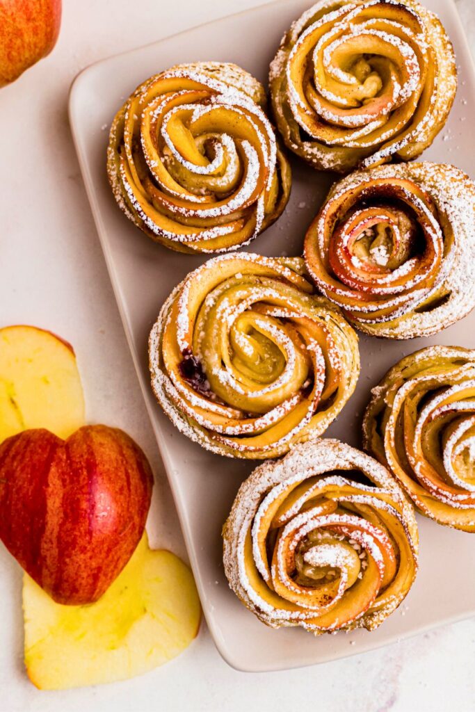 Baked apple roses on a rectangle plate, topped with powdered sugar.