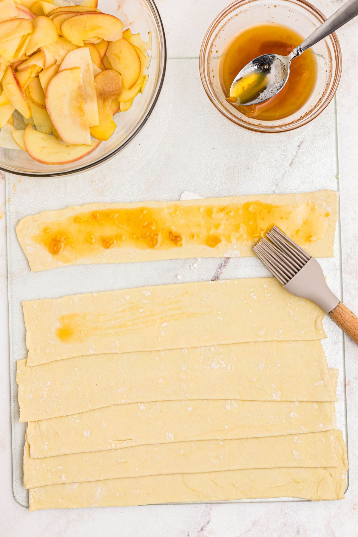 Puff pastry cut into strips being brushed with apricot jam.