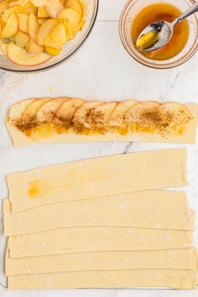 Apple slices laid overlapping across a strip of puff pastry and apricot jam. 