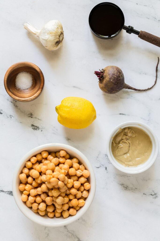 Ingredients needed to make beet hummus measured in containers and laying on the a marble table. 