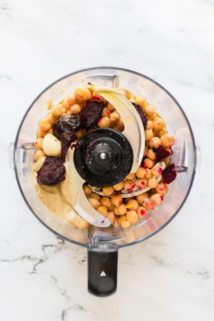 Roasted beets and other ingredients in a food processor before mixing on a marble table. 