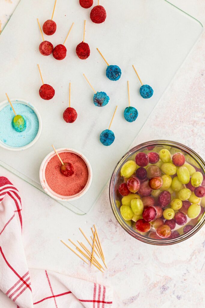 Grapes soaking in a water and being rolled in gelatin and placed on parchment paper. 