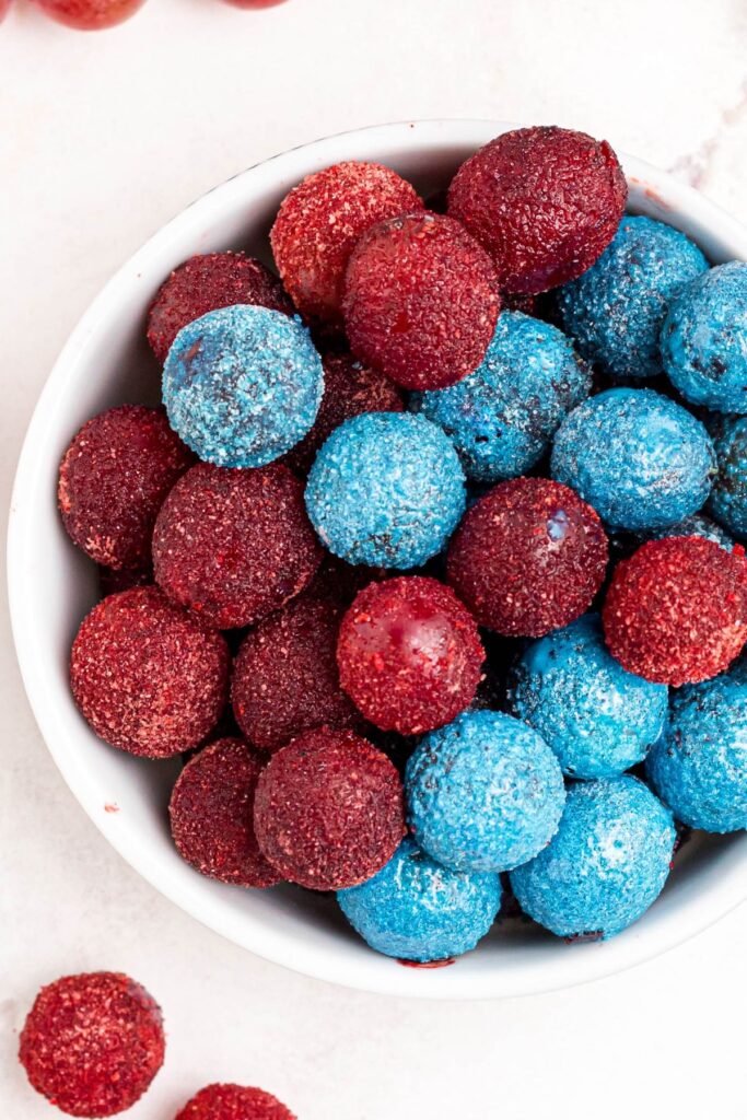 A bowl of red and blue grapes coated in flavored powders, stacked in a white bowl. 