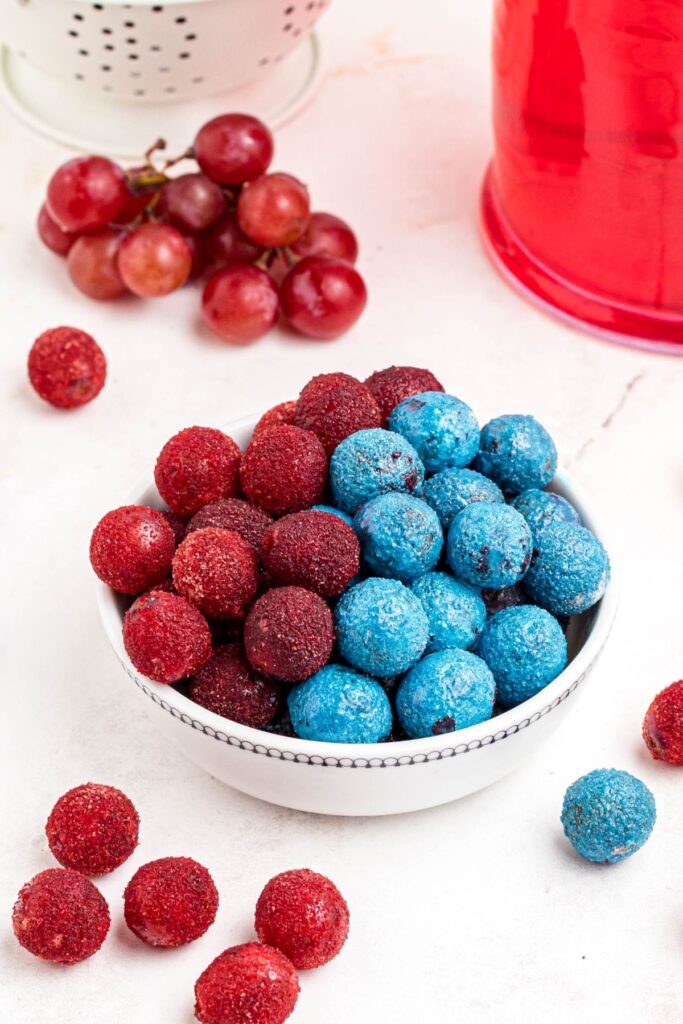 Red and blue powdered grapes stacked in a white bowl with some scattered on the table. 