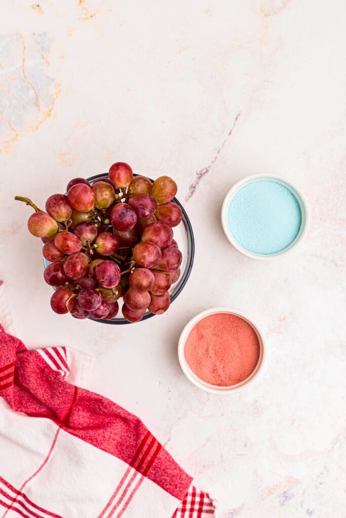 Grapes and powdered gelatin in bowls on a marble table. 