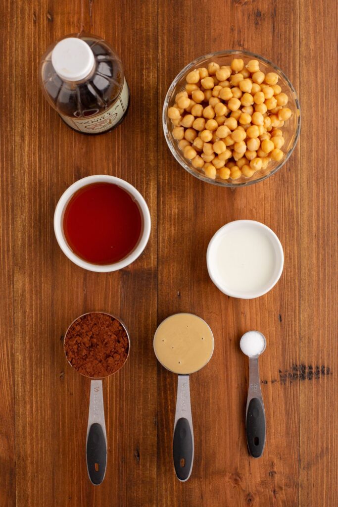 Ingredients needed to make chocolate hummus measured into containers on a wood table.