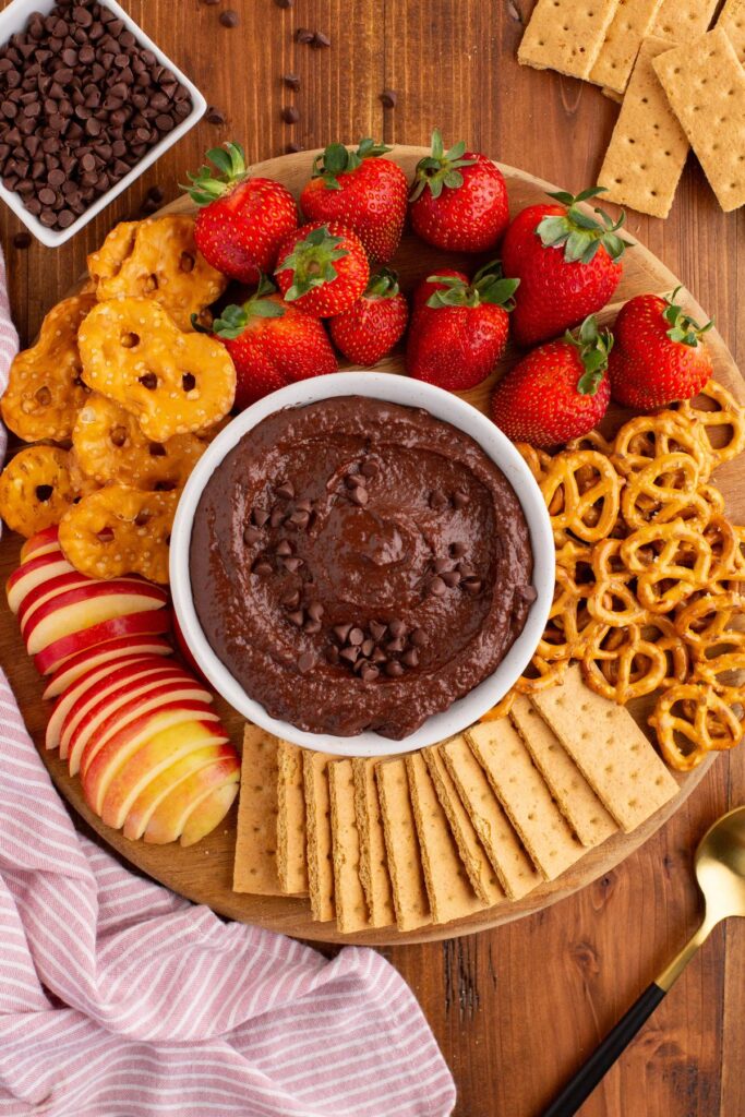 Chocolate hummus in a white bowl with dipping items around the bowl. 