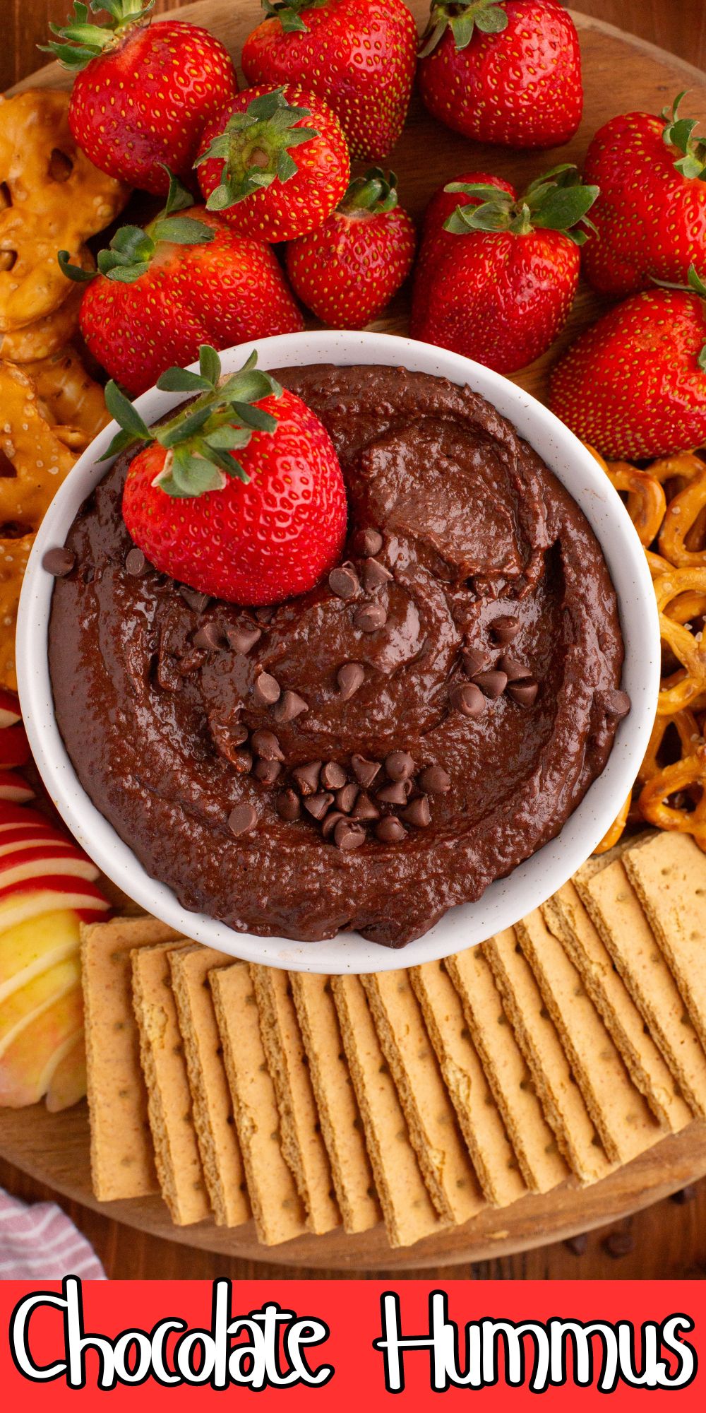 Chocolate hummus in a white bowl with a golden serving spoon in the center, with dipping items like strawberries and pretzels around the bowl.