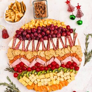 Meats, cheeses, fruits, crackers, and nuts on a Christmas charcuterie board.