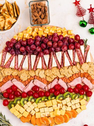 Meats, cheeses, fruits, crackers, and nuts on a Christmas charcuterie board.