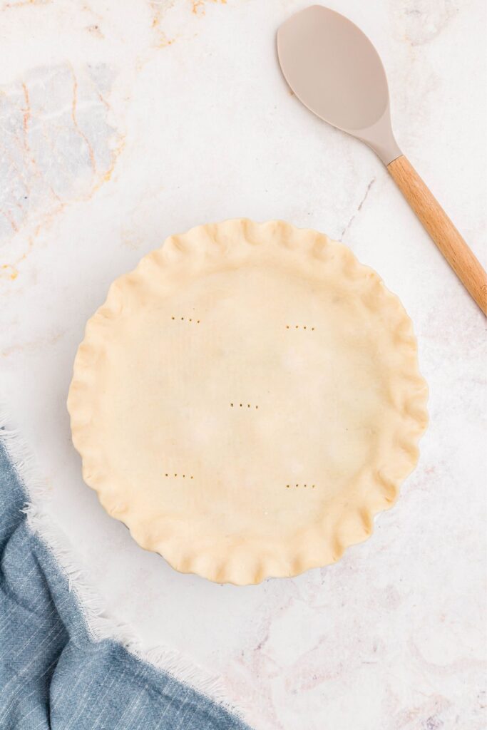 Unbaked pie topped with a pie crust with holes made by a fork. 